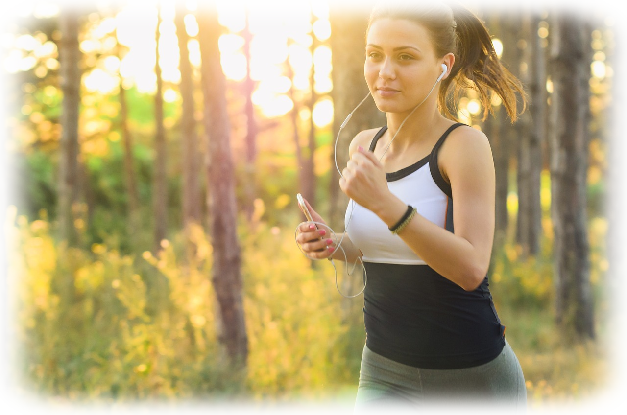 Esercizio Fisico all'Aperto: Energia e Benessere Naturale Immagine di una donna che corre all'aperto in un bosco, con le cuffie, godendo della luce del sole al tramonto. Un esempio di esercizio fisico per migliorare energia e benessere.